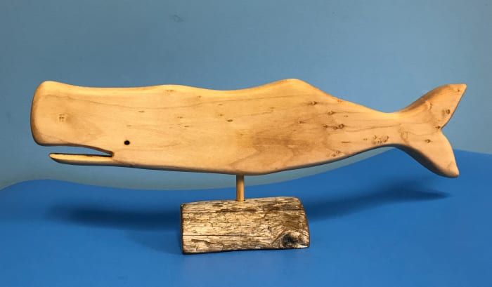 Cette baleine est en érable et repose sur un support en bois flotté