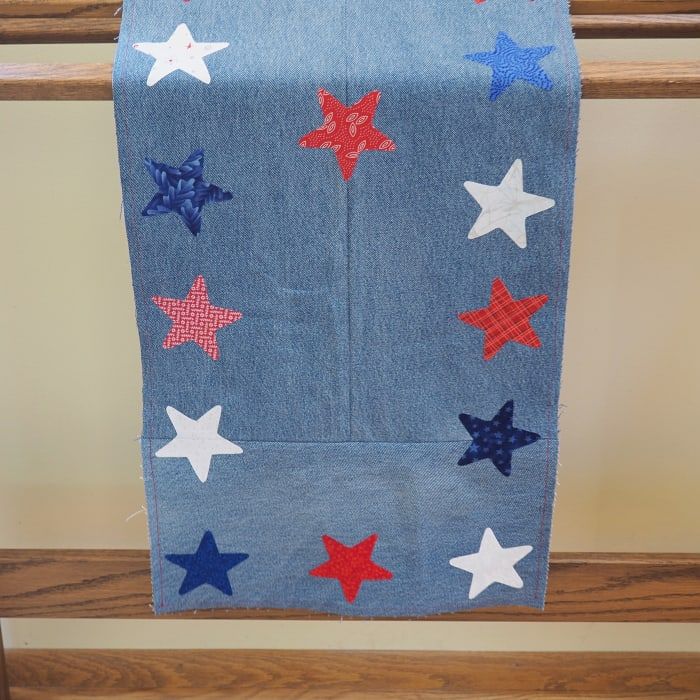 Dieser patriotische Tischläufer aus wiederverwendeten Blue Jeans und Stoffresten muss nicht nur auf einem Tisch ausgestellt werden. Hängen Sie es für zusätzliche Farbe über ein Quiltgestell.