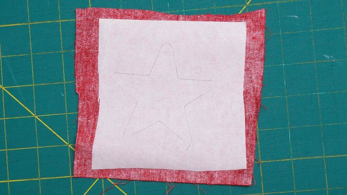 Korzystając z szablonu gwiazdy, narysuj kształt na papierowej stronie topliwej wstęgi, która została już nałożona na tkaninę.
