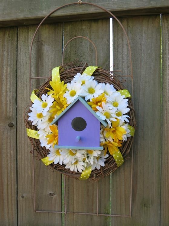 ein charmanter Willkommenskranz mit einem Gartenzaunstück, einem Vogelhaus und einigen künstlichen Blumen