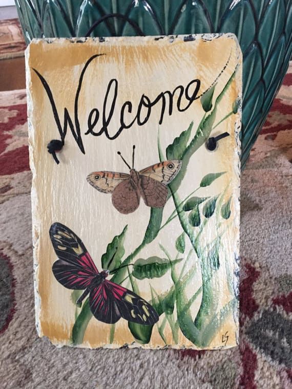 Puede usar una mezcla de pintura y recortes de decoupage para crear una pizarra de bienvenida fabulosa para su hogar (¡las mariposas son difíciles de pintar, pero fáciles de decoupage!).
