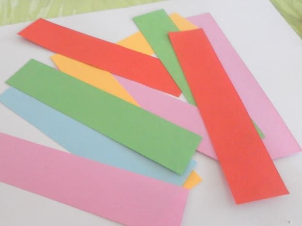 Цветна занаятчийска хартия, нарязана на ивици и готова за изработване на хартиени сърца.
