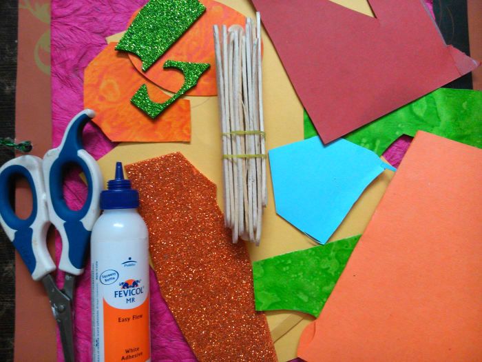 Acrylfarbe, ein Pinsel, sechs Eisstangen, ein Klebestift, eine Schere, ein paar Blätter farbiges, strukturiertes und glänzendes Papier.