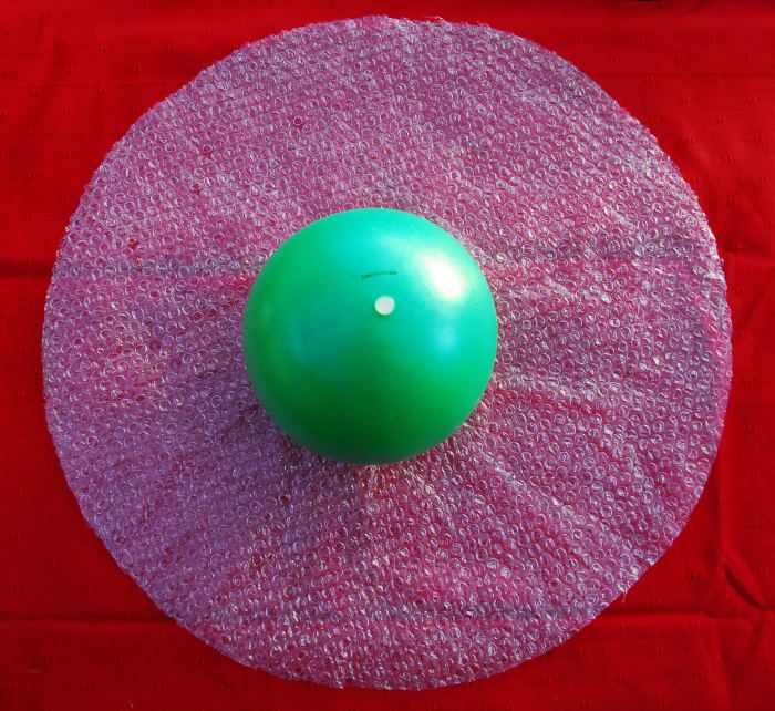 Schneiden Sie einen Kreis aus der Luftpolsterfolie. Der Durchmesser sollte ausreichen, damit Sie die Kugel mit offenem Ende kurz vor dem Ventil oder Knoten im Ballon in die Luftpolsterfolie einwickeln können. Legen Sie sie auf ein Handtuch oder alternativ eine Luftpolsterfolie.