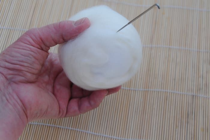 Coloque la mecha de lana blanca en la bola con una aguja de fieltro.