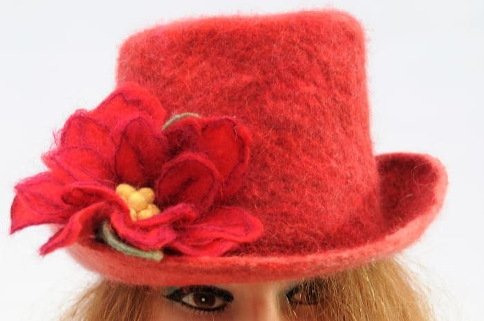 Un sombrero de fieltro rojo esperando una banda de sombrero con la adición de una flor de fieltro.