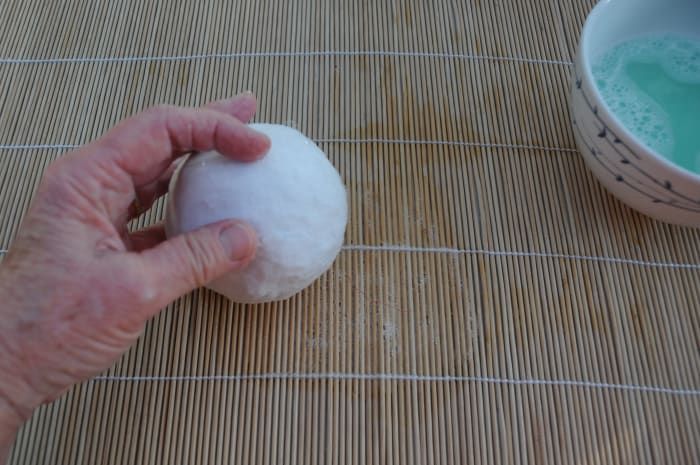 Rollen Sie den mit Wolle bedeckten Ball vorsichtig auf die Bambusmatte, um die Wollfasern zu glätten.